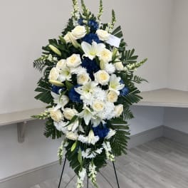 Standing floral spray with white roses, lilies, and blue chrysanthemums on an easel