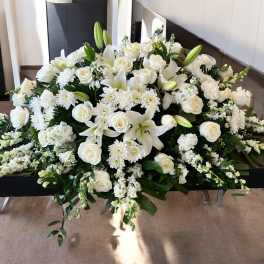 White floral casket spray with roses, lilies, and chrysanthemums