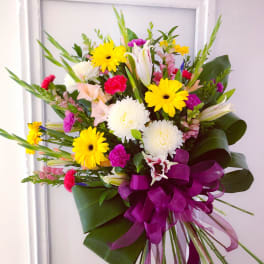 Colorful mixed bouquet with yellow daisies, white lilies, and a purple ribbon