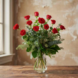 Tall bouquet of red roses with abundant greenery arranged in a clear glass vase.