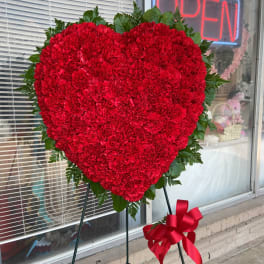 Heart-shaped red carnation standing spray with a ribbon on an easel