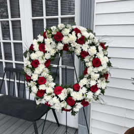 Red roses and white chrysanthemums arranged in a large wreath on a stand
