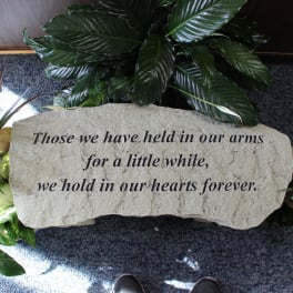 Memorial stone with engraved sympathy message surrounded by green plants