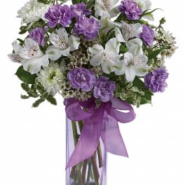 Purple and white bouquet in a clear square vase with a ribbon