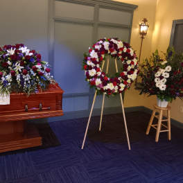 Funeral casket spray, standing wreath, and floral vase arrangement in red, white, and purple