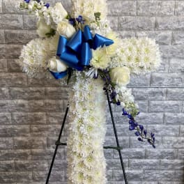 White floral standing spray with blue ribbon and purple accents on an easel