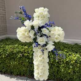 White rose cross-shaped floral tribute with blue accents on an easel