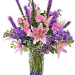 Pink lilies and roses in a clear glass vase with purple flowers