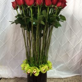 Tall vase arrangement of red roses with green orchids at the base