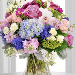 Mixed bouquet of pink, purple, blue, and white flowers in a clear glass vase