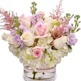 Pastel bouquet of roses, hydrangeas, and lavender flowers in a clear glass vase