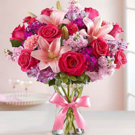 Pink roses and lilies arranged in a glass vase with a pink ribbon