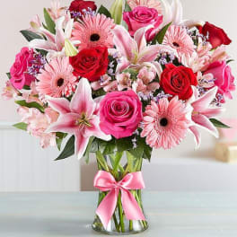 Bouquet of pink and red flowers in a glass vase with a pink ribbon