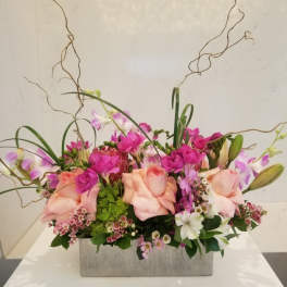 Pink roses and orchids in a rectangular gray vase with curly branches