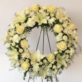 Cream floral wreath on a black stand with roses and lilies