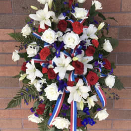 Standing floral spray with red and white roses, lilies, and ribbon streamers