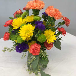Mixed bouquet of yellow daisies, carnations, and purple blooms in a glass vase