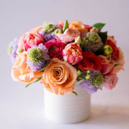 Mixed bouquet of peach, pink, and purple flowers in a white vase