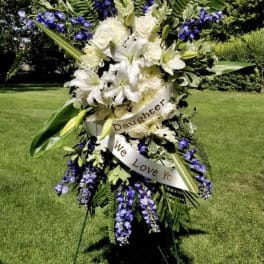 Standing floral spray with white lilies and purple flowers on an easel