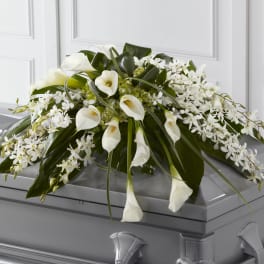 White calla lilies and orchids arranged on a gray casket