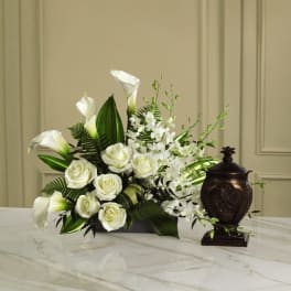White roses and calla lilies arranged with white orchids in a low vase