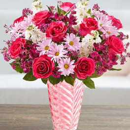 Pink and white mixed bouquet with roses and daisies in a tall pink glass vase