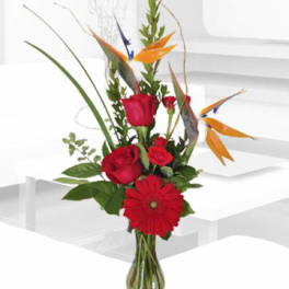 Red roses and a gerbera daisy in a glass vase with tropical accents