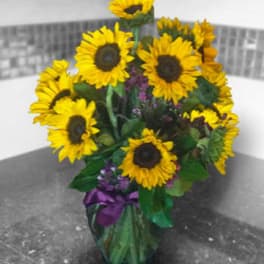 Bouquet of yellow sunflowers in a glass vase with purple ribbon