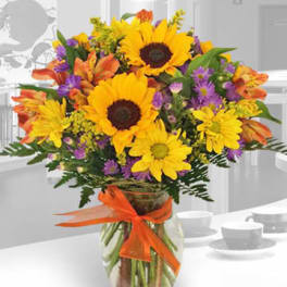 Bouquet of sunflowers, daisies, and orange flowers in a glass vase
