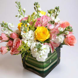Mixed bouquet of pink, white, and yellow flowers in a striped square box