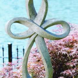 Stone sculpture with interlocking loops beside a pond and pink shrubs