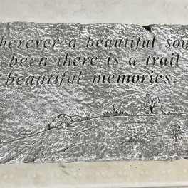 Rectangular gray memorial stone engraved with a sentimental quote and small landscape motifs.