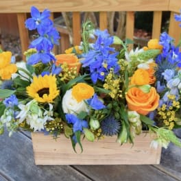 Mixed bouquet in a wooden box with blue, yellow, and orange flowers