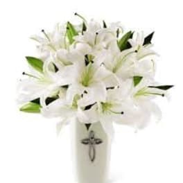 White lilies arranged in a tall white vase with a cross emblem