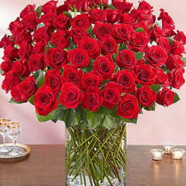Large bouquet of red roses arranged in a clear glass cylinder vase on a table
