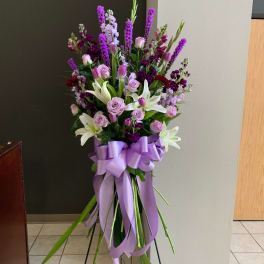 Tall bouquet of pink and purple flowers with white lilies and a lavender ribbon