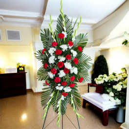 Standing floral spray with red and white carnations on a palm backdrop