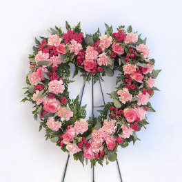 Heart-shaped floral wreath with pink roses and carnations on a stand