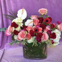 Mixed pink and red rose arrangement in a clear glass vase with white anthuriums