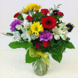 Mixed bouquet of colorful flowers in a glass vase with a yellow ribbon