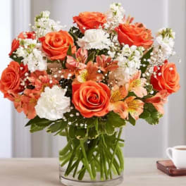 Orange roses and white flowers arranged in a clear glass vase