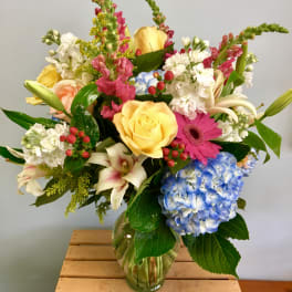 Mixed bouquet of roses, hydrangea, lilies, and gerbera daisies in a glass vase