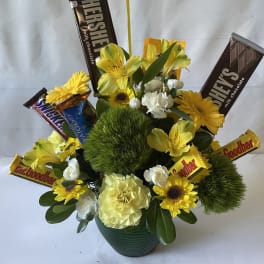 Yellow flowers and chocolate bars arranged in a green pot.