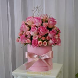Pink roses arranged in a round pink hatbox with a satin bow