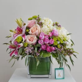 Mixed pink and white flower arrangement in a glass vase with a small necklace box beside it