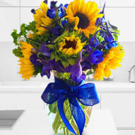 Bouquet of yellow sunflowers and purple flowers in a glass vase with a blue ribbon