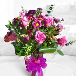 Pink roses and purple flowers in a glass vase with a ribbon