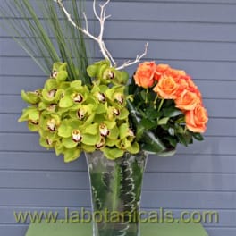 Orange roses and green orchids in a tall glass vase