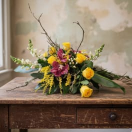 Low arrangement of yellow roses, pink orchids, and white snapdragons on a rustic wooden table