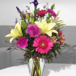 Mixed bouquet with pink gerbera daisies and yellow lilies in a clear vase